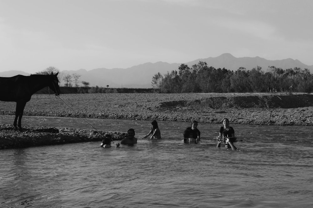 Un gruppo di persone in piedi in un fiume accanto a un cavallo