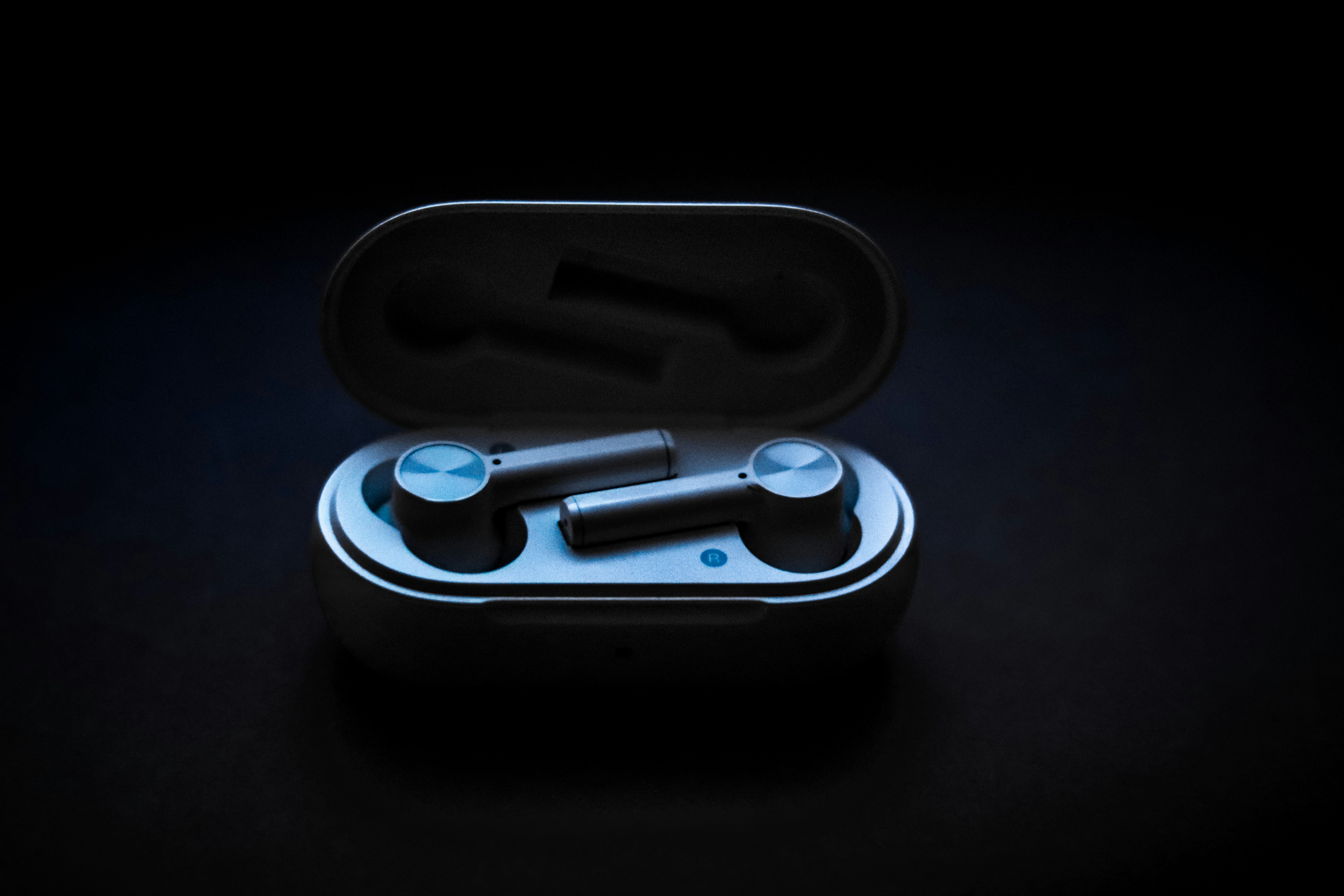 Premium wireless earbuds in case on dark background with blue accent lighting