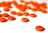 A collection of orange pills scattered on a white surface. Several pills are blurred in the background, while one pill in the foreground is in sharp focus with numbers printed on it.