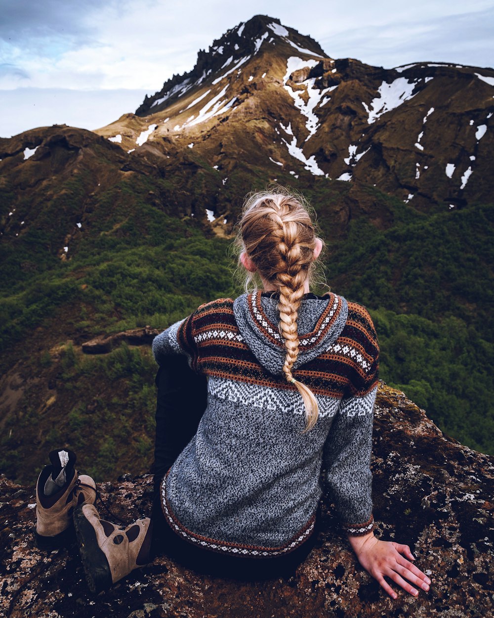 a woman sitting on top of a mountain next to a pair of shoes