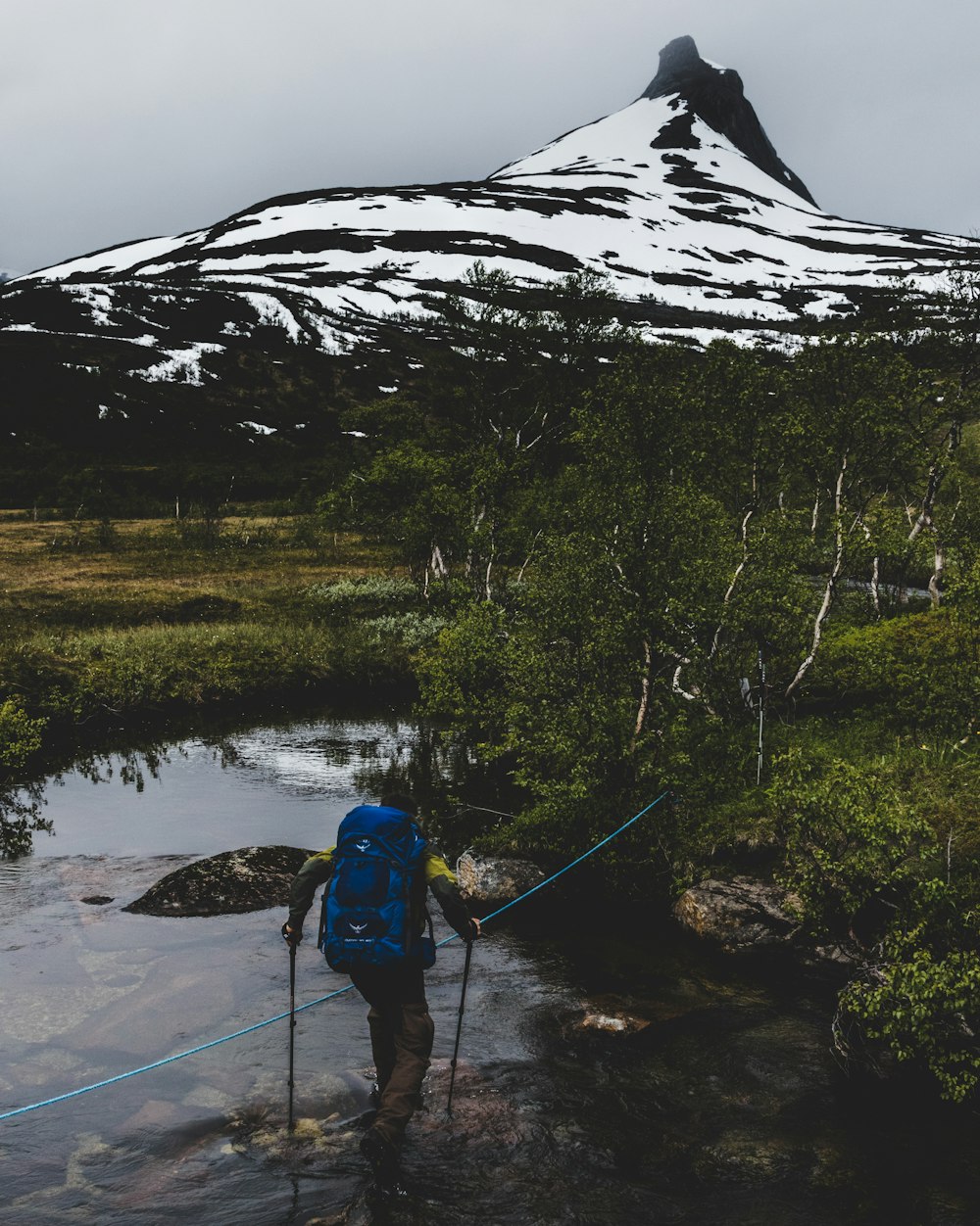 a person with a backpack crossing a stream in front of a mountain