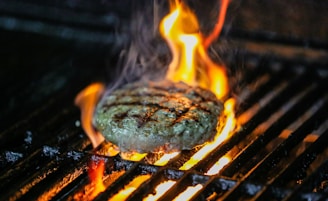 A close-up shot of a sizzling burger on the grill with flames licking the edges.