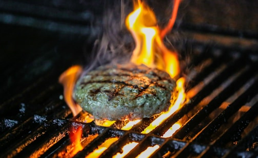 A close-up shot of a sizzling burger on the grill with flames licking the edges.