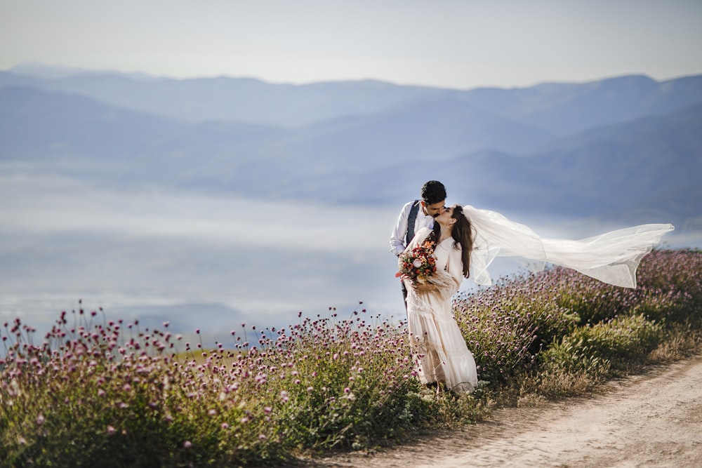 a bride and groom kissing on top of a hill