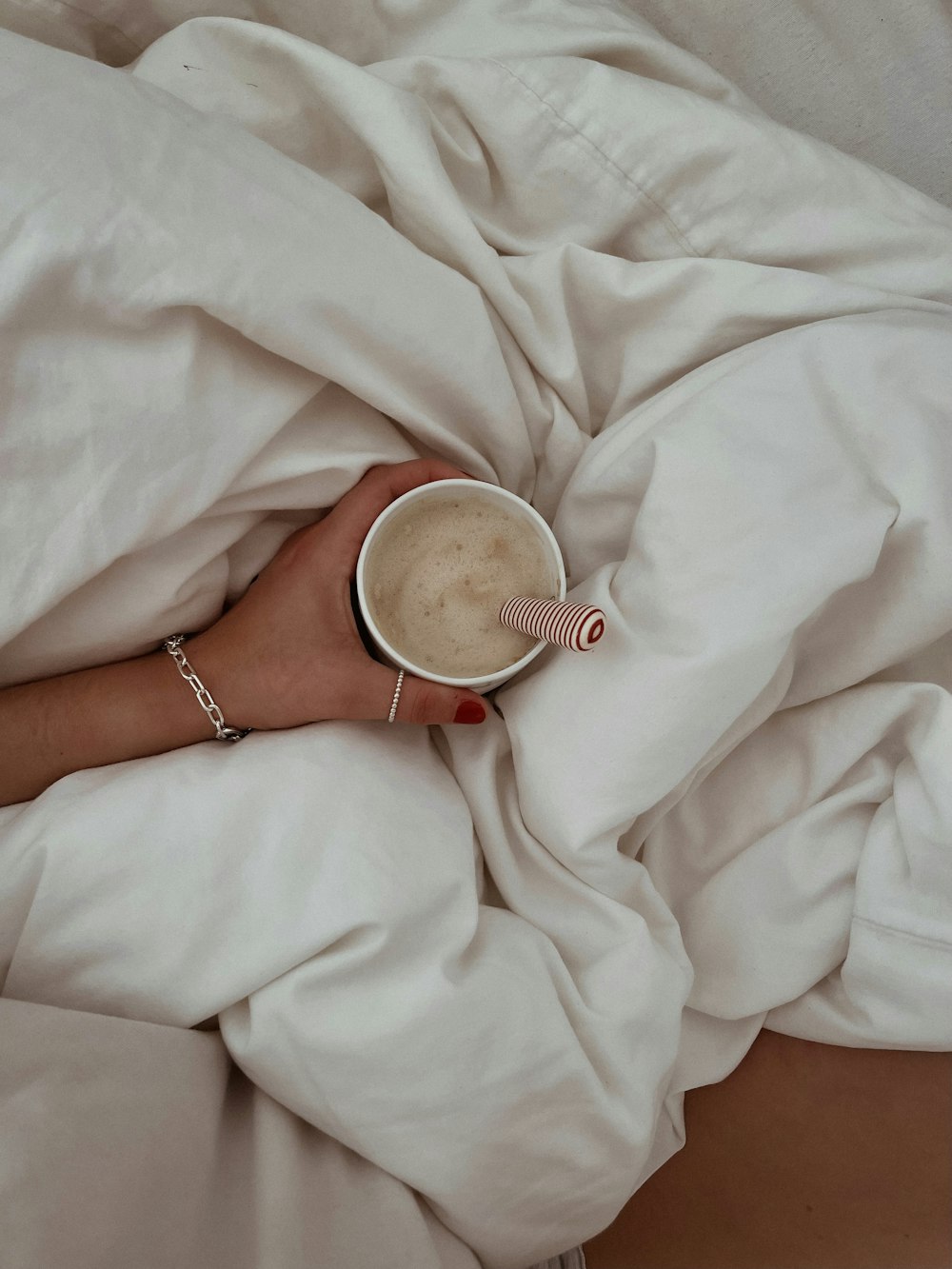 a woman is holding a cup of coffee in bed