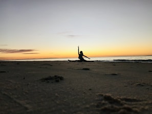 Sunset over a San Diego beach with a silhouette of a person doing assisted stretching