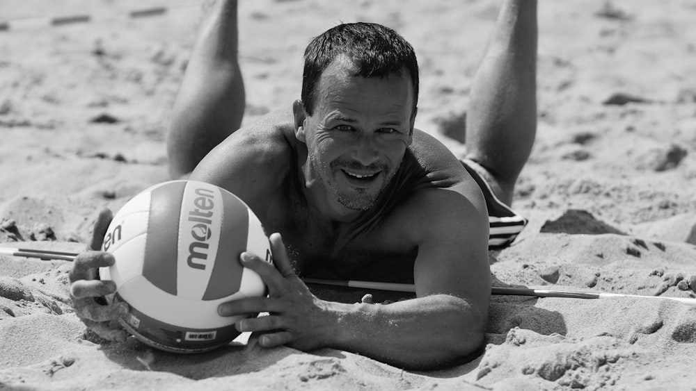 a man laying on top of a sandy beach holding a volleyball