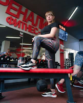 A confident woman lifting weights in the dedicated ladies fitness area, bathed in soft purple glow.