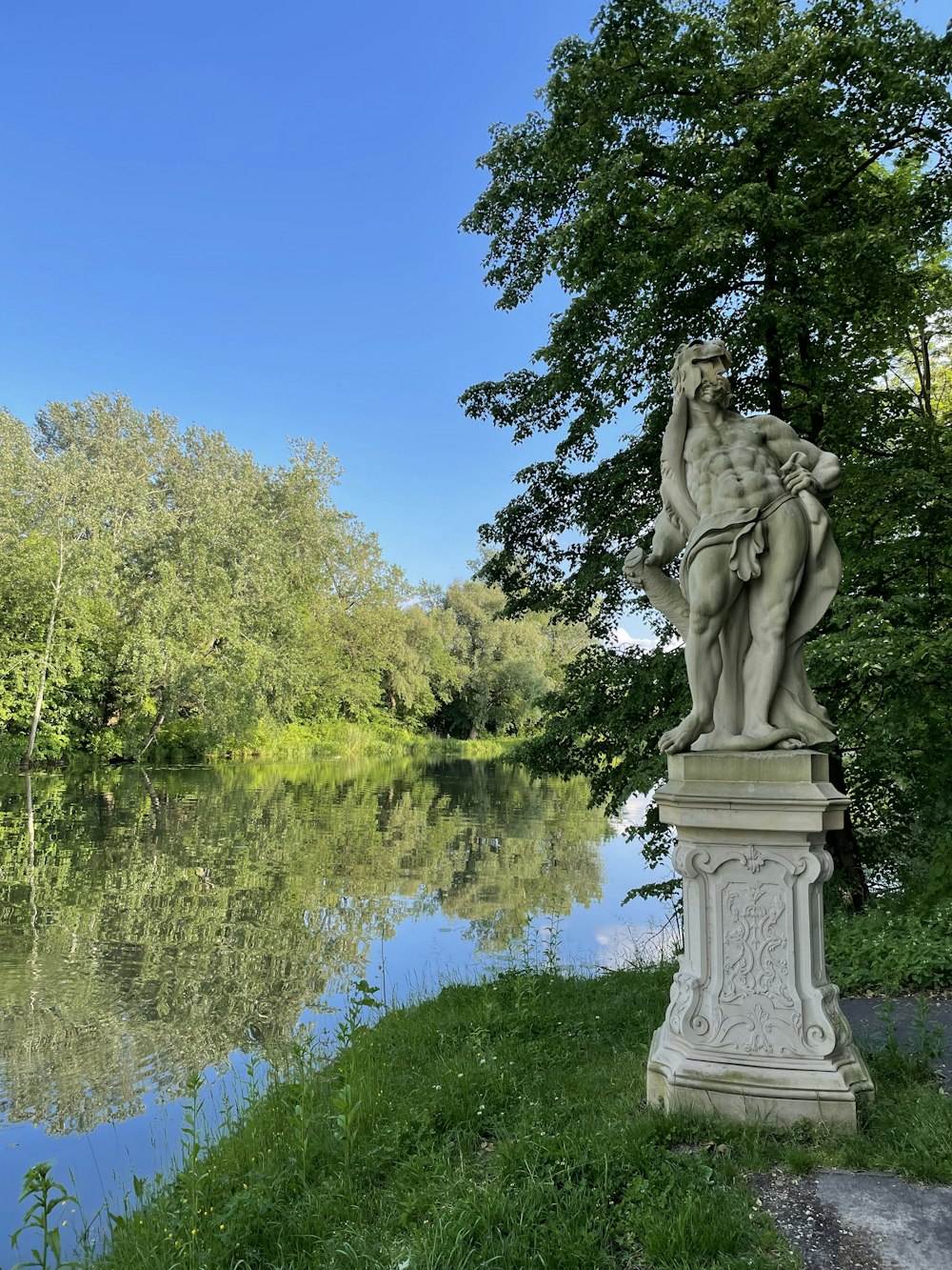 uma estátua sentada no topo de um campo verde exuberante ao lado de um rio