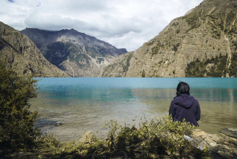 a person sitting on a rock near a lake