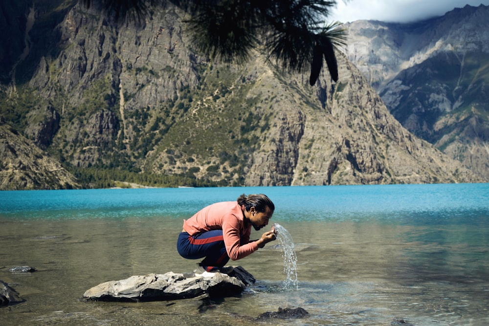 Una persona arrodillada sobre una roca cerca de un cuerpo de agua