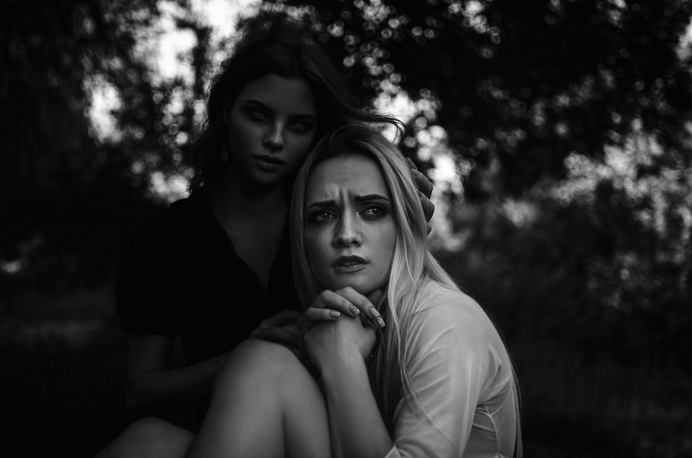 two women sitting next to each other in a forest