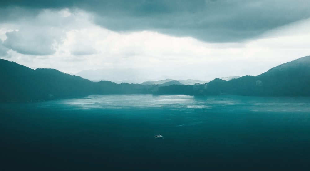 a body of water surrounded by mountains under a cloudy sky