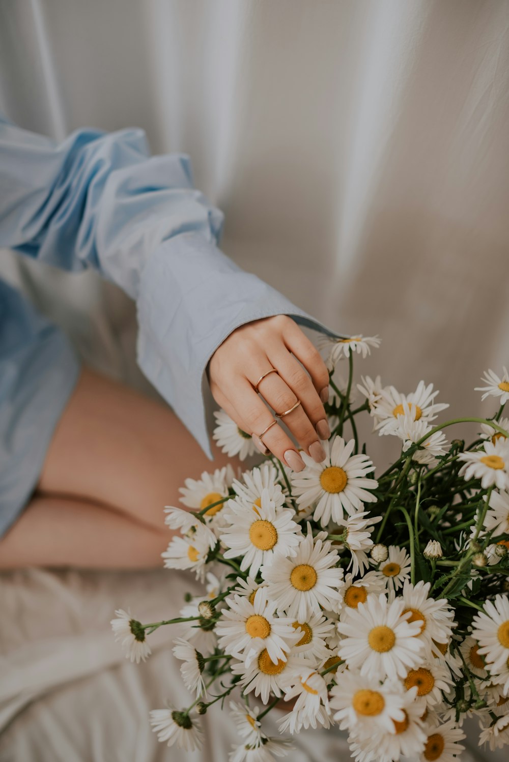 a woman sitting on a bed with a bouquet of daisies