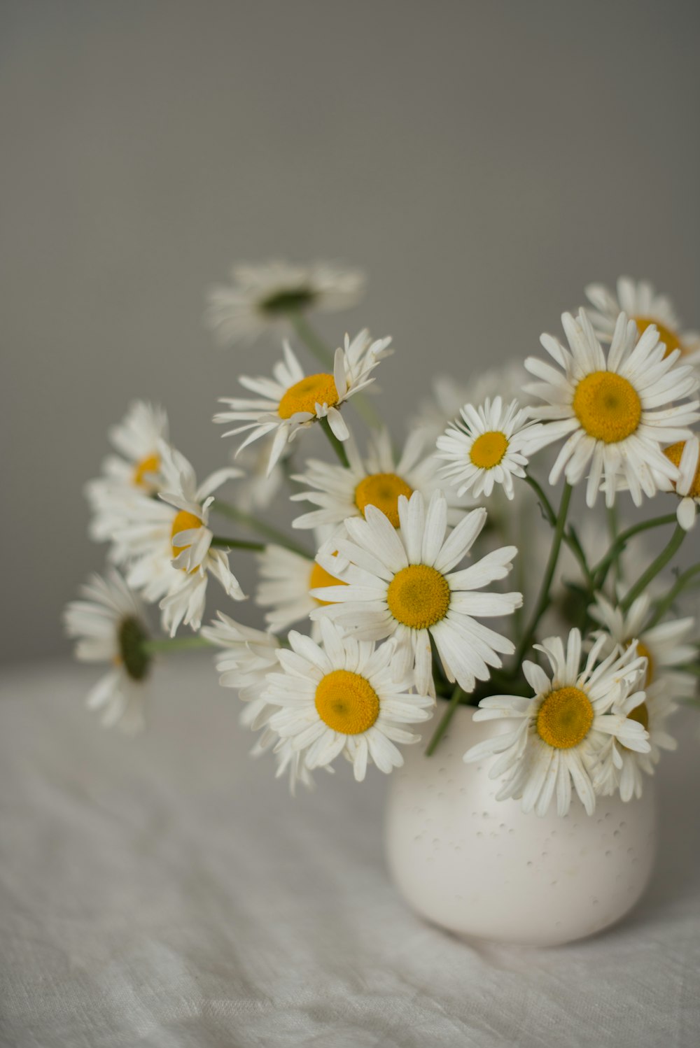 a white vase filled with white and yellow flowers