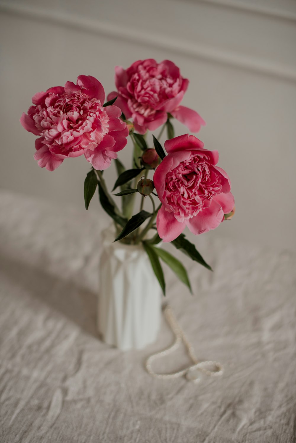 a white vase filled with pink flowers on top of a bed