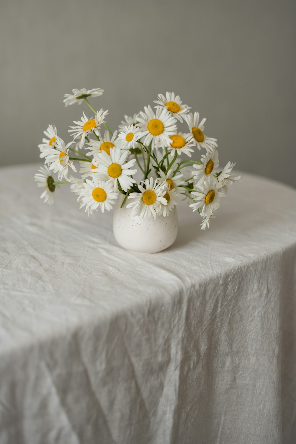 eine weiße Vase gefüllt mit gelben und weißen Gänseblümchen