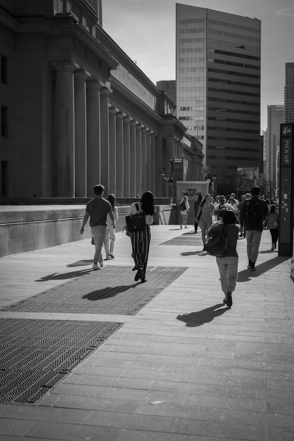 a group of people walking down a sidewalk next to tall buildings