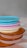 A stack of round, plastic lids in various colors including blue, pink, cream, and amber is neatly arranged on a surface. The lids are translucent and each layer is visible through the others, creating a subtle blending of shades. The background is softly blurred, emphasizing the focus on the lids.