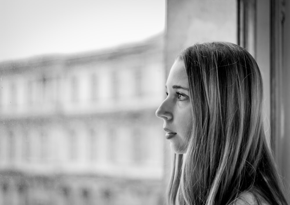 a black and white photo of a woman looking out a window