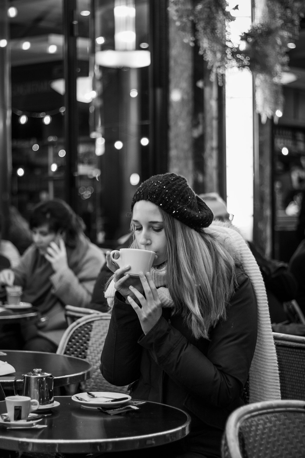 a woman sitting at a table drinking a cup of coffee