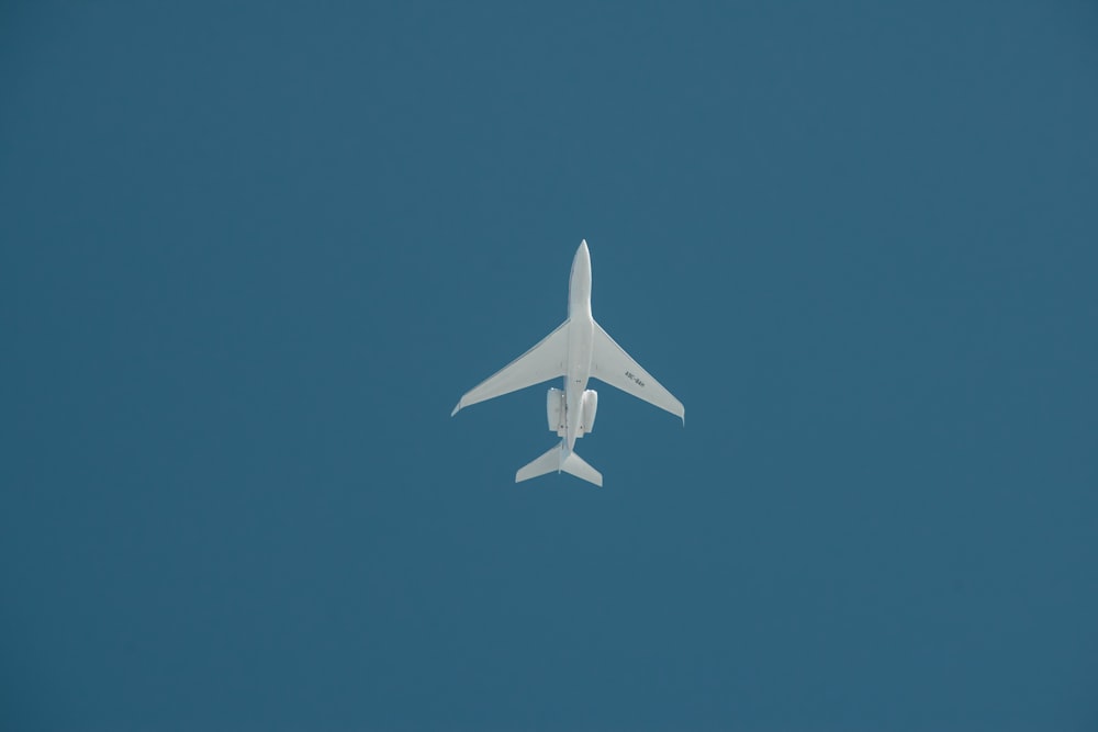 a white jet flying through a blue sky