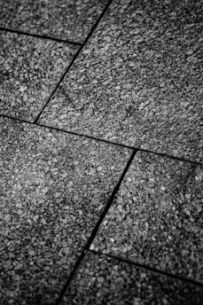 Close-up view of textured stone tiles arranged in a geometric pattern with visible seams. The surface is rough and speckled, creating an intricate design.