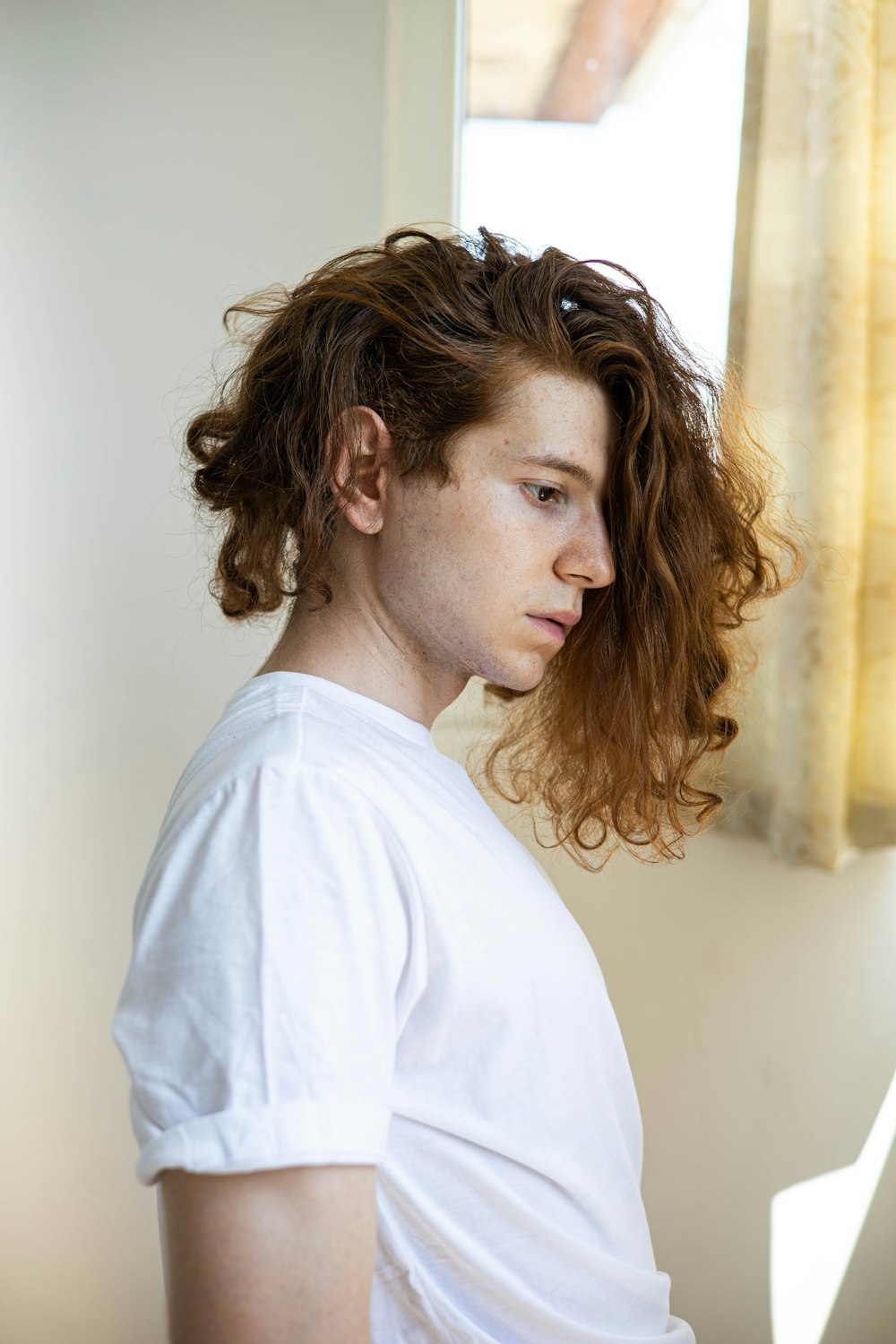 a man with curly hair standing in front of a window