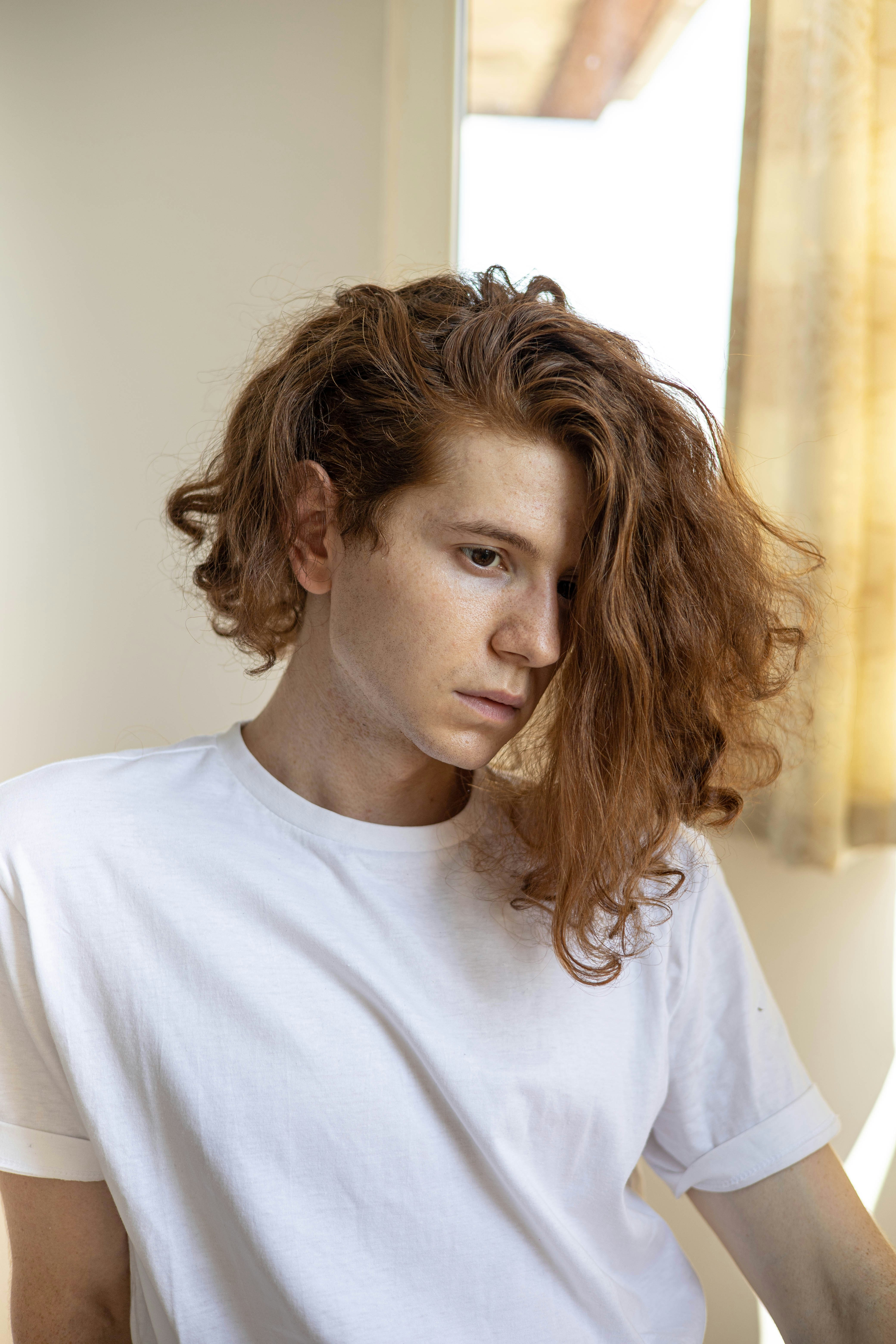 a young man with red hair sitting in front of a window
