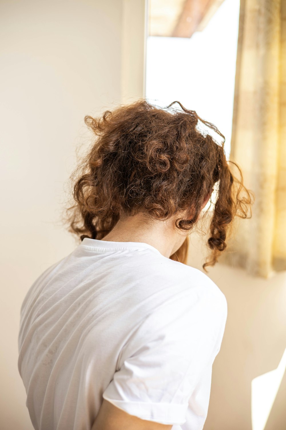 a woman with curly hair sitting in front of a window