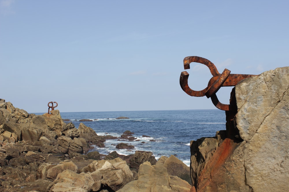 a rusted metal sculpture sitting on top of a rocky cliff next to the ocean