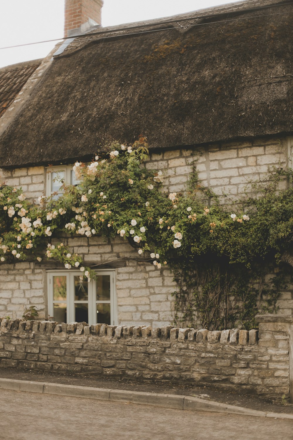 a brick building with a thatched roof and flowers growing on it