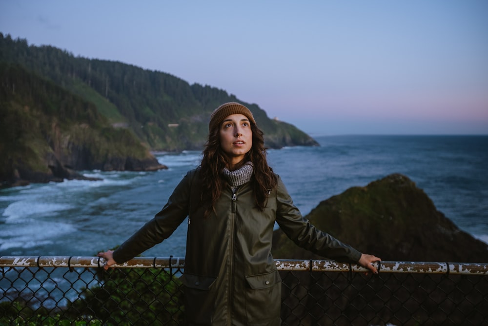 a woman standing on a fence near the ocean