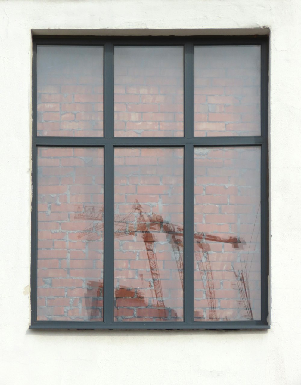 a window with a brick wall and a crane reflected in it
