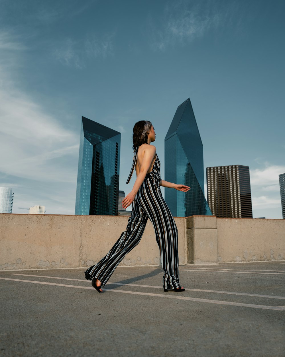 a woman walking across a parking lot next to tall buildings