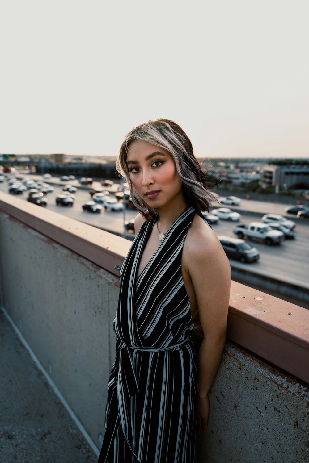 a woman leaning against a wall near a parking lot