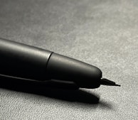 Close-up of a matte black pen with subtle metallic accents, poised elegantly on textured paper.
