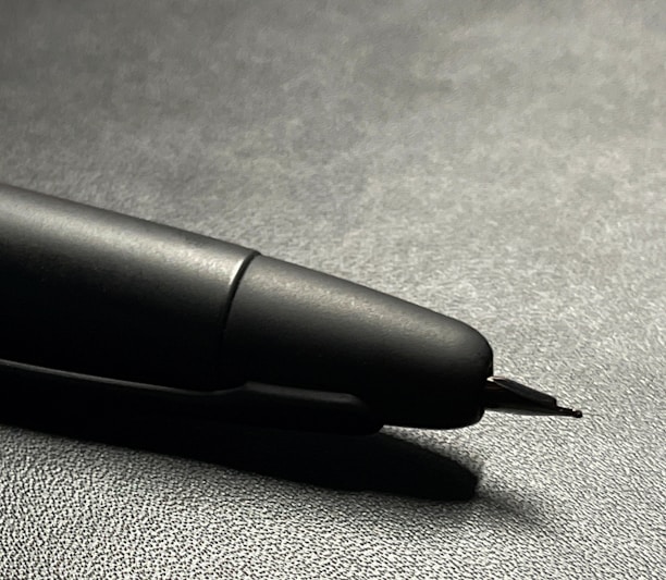 Close-up of a sleek, black ink pen resting on a wooden desk with soft natural light highlighting its smooth finish.