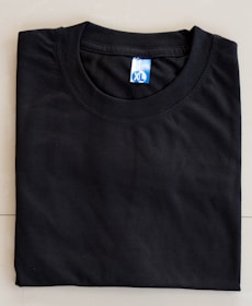 A neatly folded black T-shirt with a blue size label marked XL on a light-colored surface.