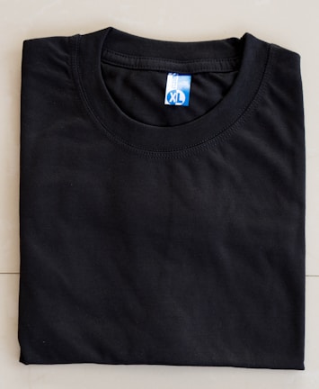 A neatly folded black T-shirt with a blue size label marked XL on a light-colored surface.