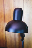 Elegant black-framed lamp casting warm light over a simple wooden desk.