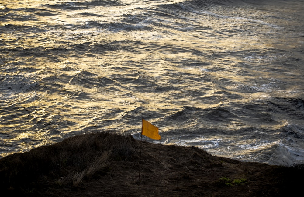 a yellow flag sitting on top of a cliff near the ocean