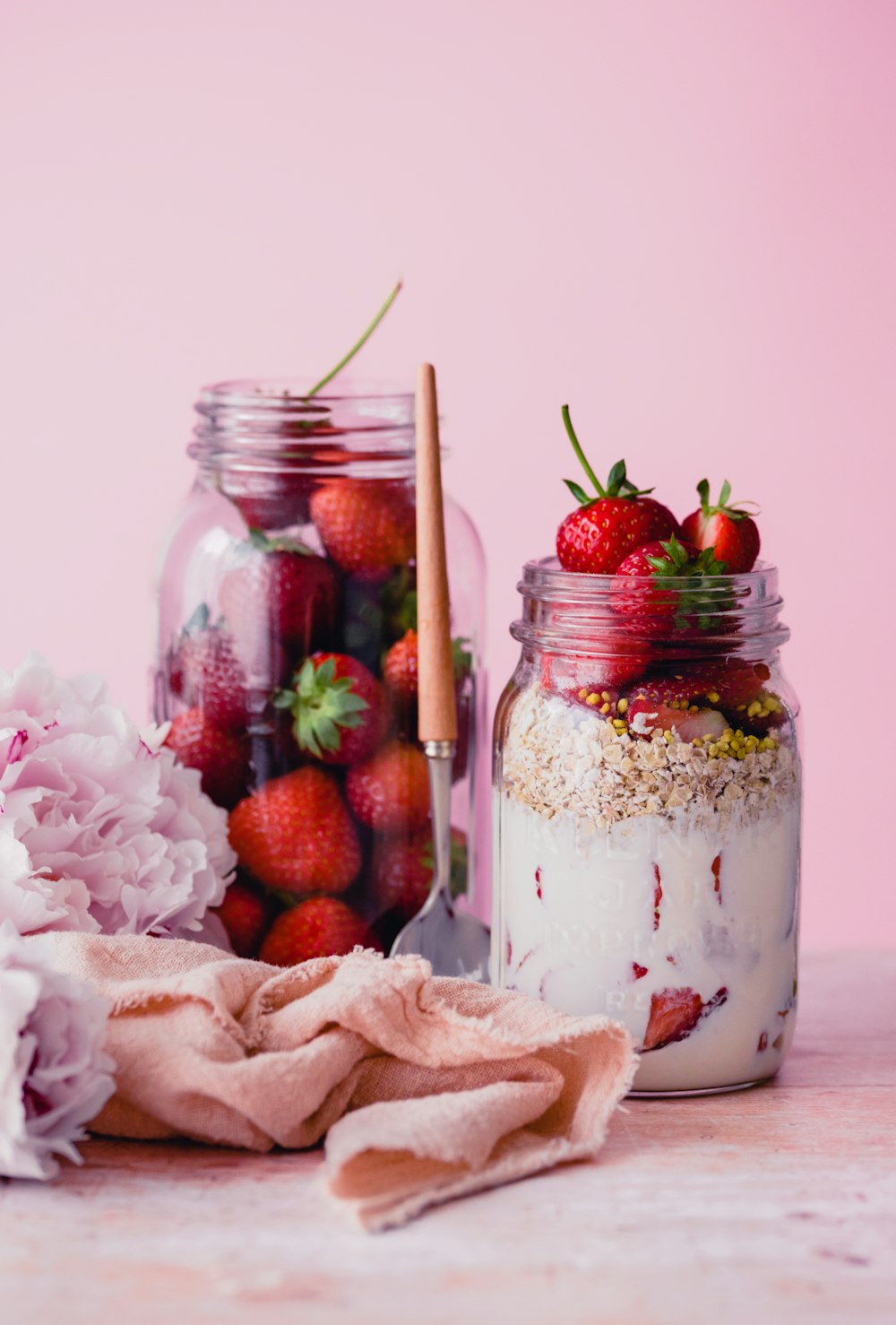 two jars filled with strawberries and granola on a table