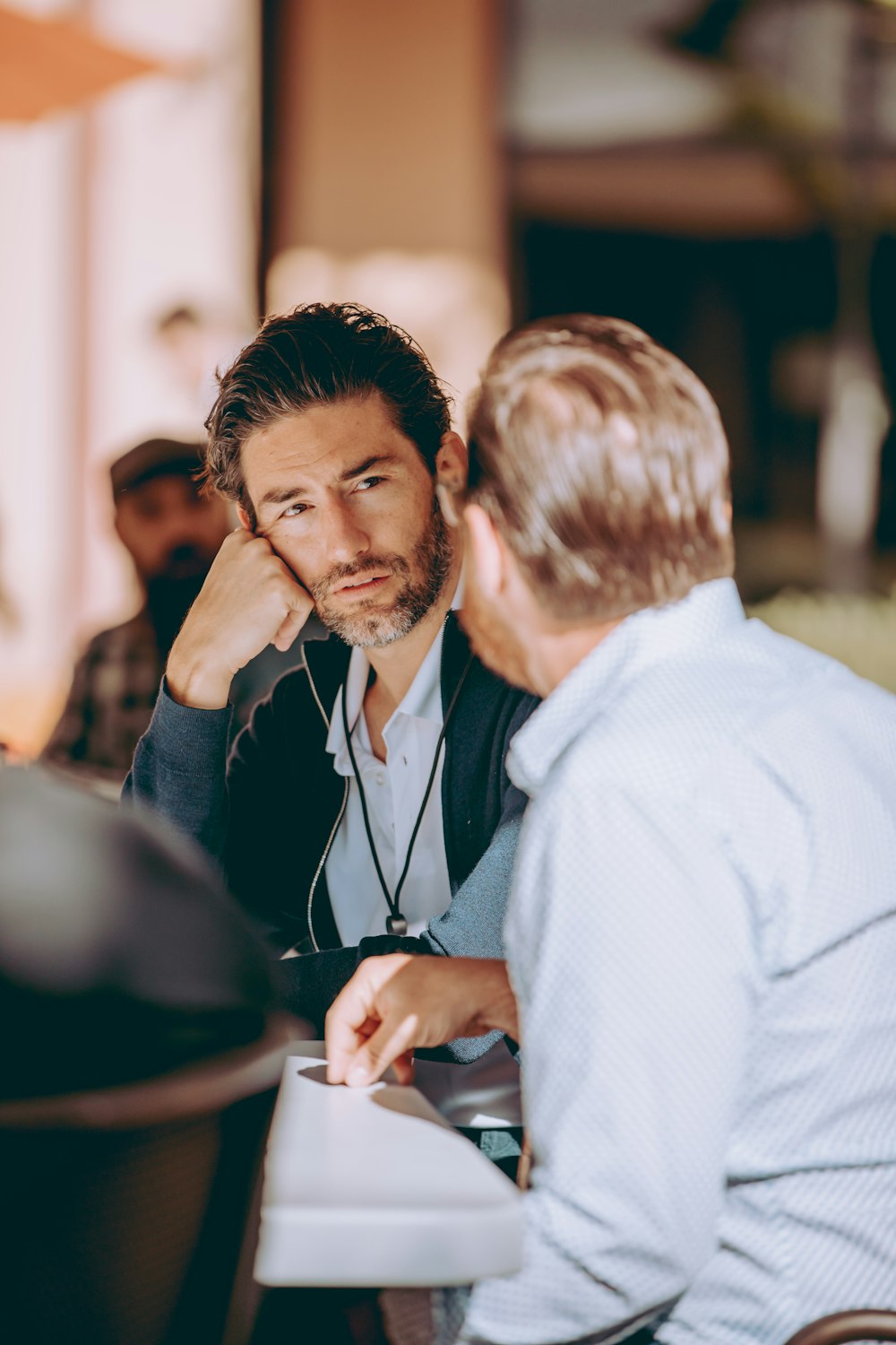 deux hommes assis à une table qui se parlent