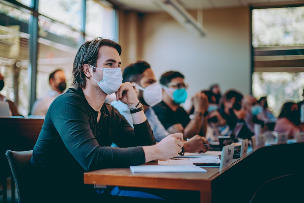 a group of people sitting at a table wearing face masks