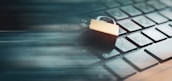 A closed padlock rests on top of a computer keyboard, symbolizing security. The image incorporates a motion blur effect, suggesting speed or data movement.