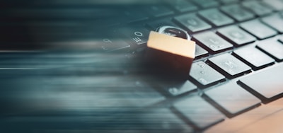 A closed padlock rests on top of a computer keyboard, symbolizing security. The image incorporates a motion blur effect, suggesting speed or data movement.