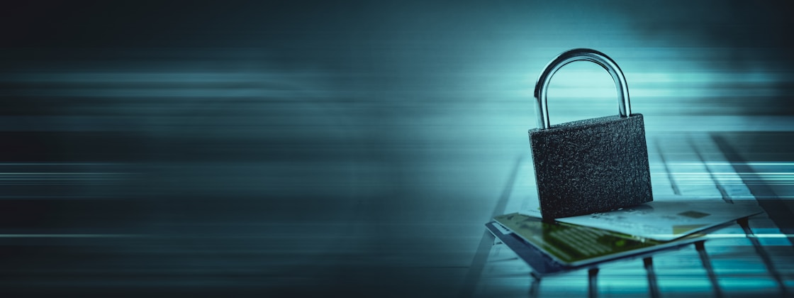 A padlock sits atop a stack of credit cards on a keyboard, with a bluish hue and digital streaks in the background, suggesting themes of digital security and privacy.