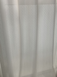 A close-up view of light-colored curtains with vertical pleats, allowing diffused light to pass through.