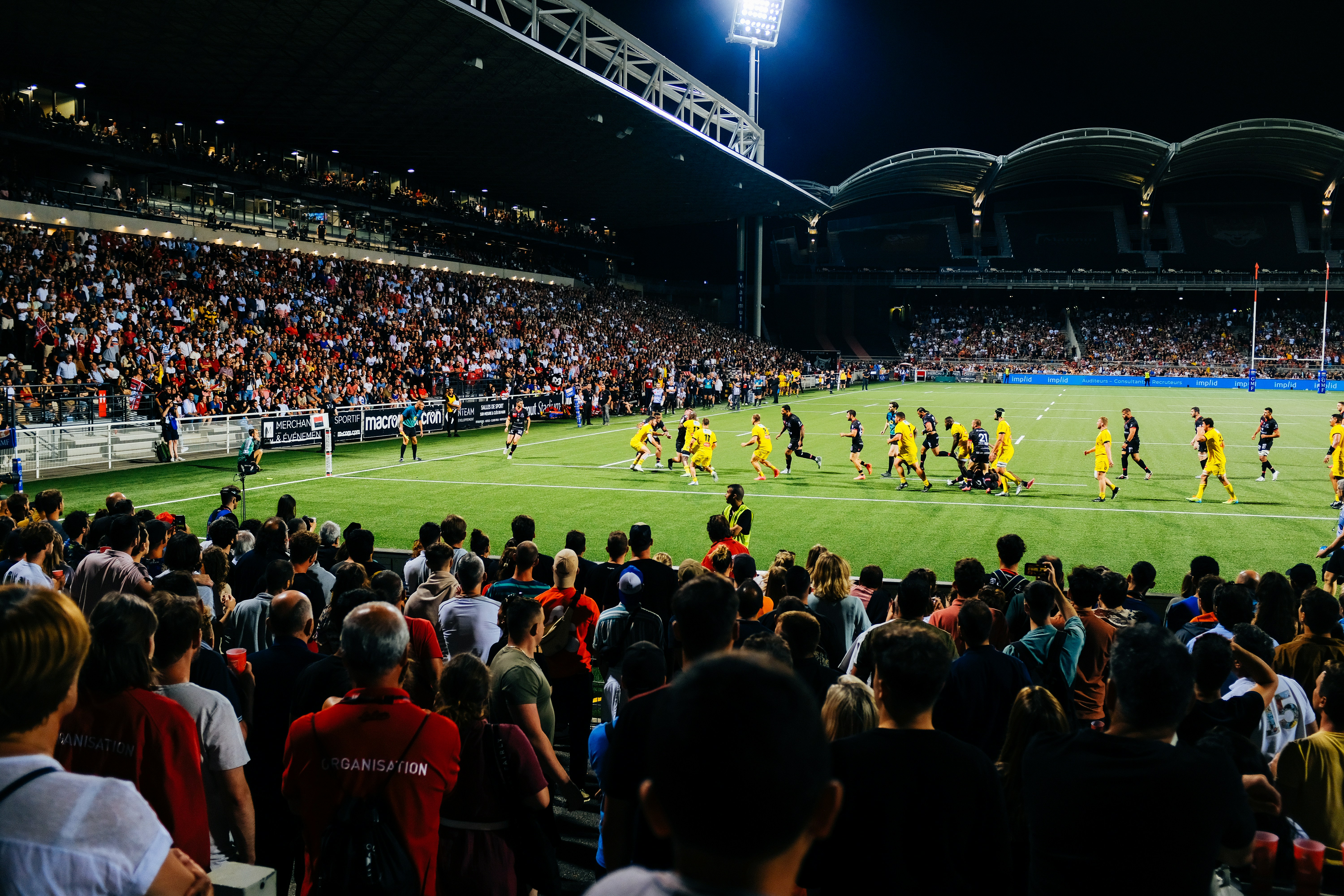 Rugby players in green jerseys on a stadium field under bright floodlights, action-packed match atmosphere